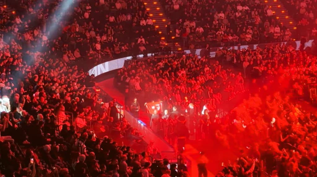 Oktagon 80'de dolu bir arenaya yukarıdan bakış: kırmızı ışık, duman ve Türk bayraklı bir taraftar.