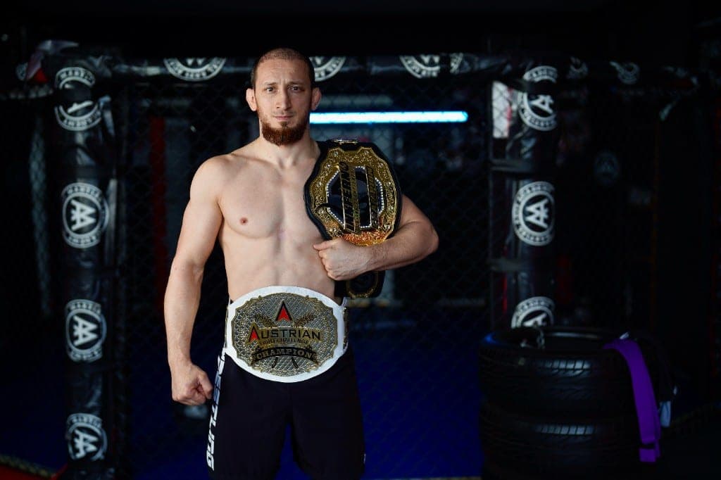 Gökhan Aksu im Käfig mit den Championship-Gürteln der Austrian Fighting Championship und Innferno
